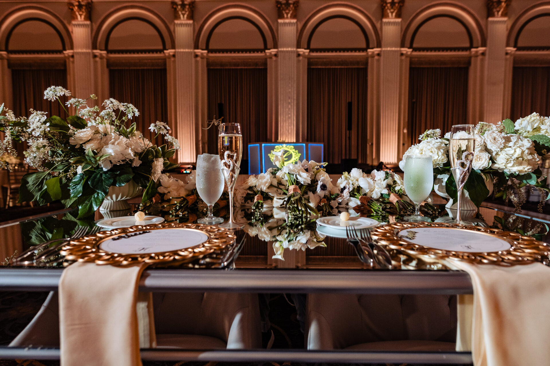Couple’s head table decorated with white floral arrangements and gold-plated plates inside the ballroom at The Ben wedding reception.