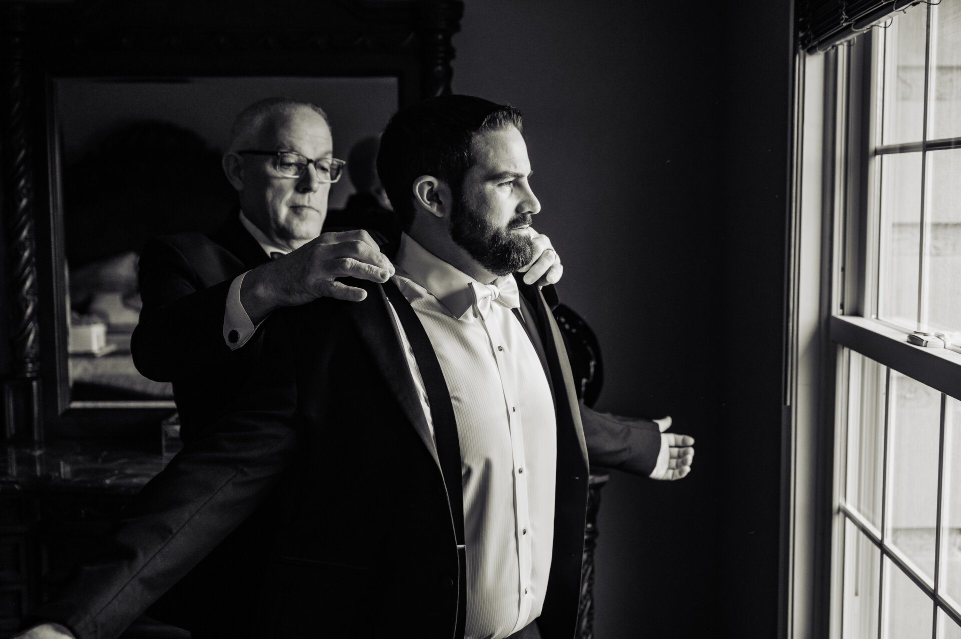 Father helping groom put on his coat during wedding preparation