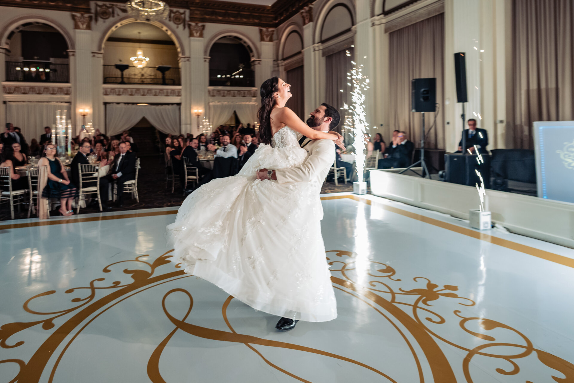 Groom lifts the bride during their first dance on the ballroom floor as sparklers ignite at The Ben wedding reception.
