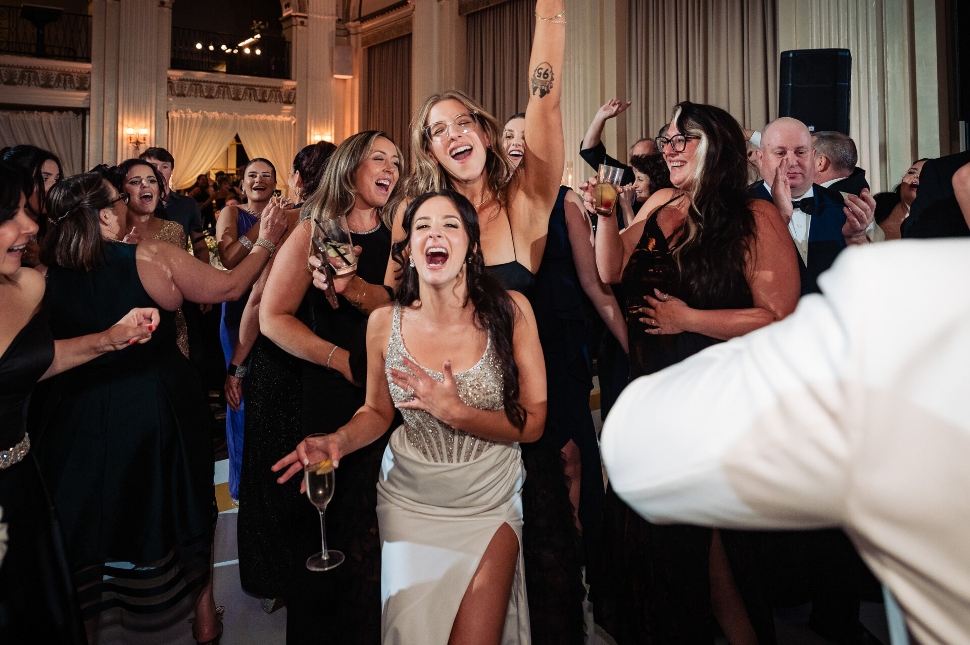 Bride laughing and singing with friends while holding champagne during the wedding reception at The Ben ballroom.