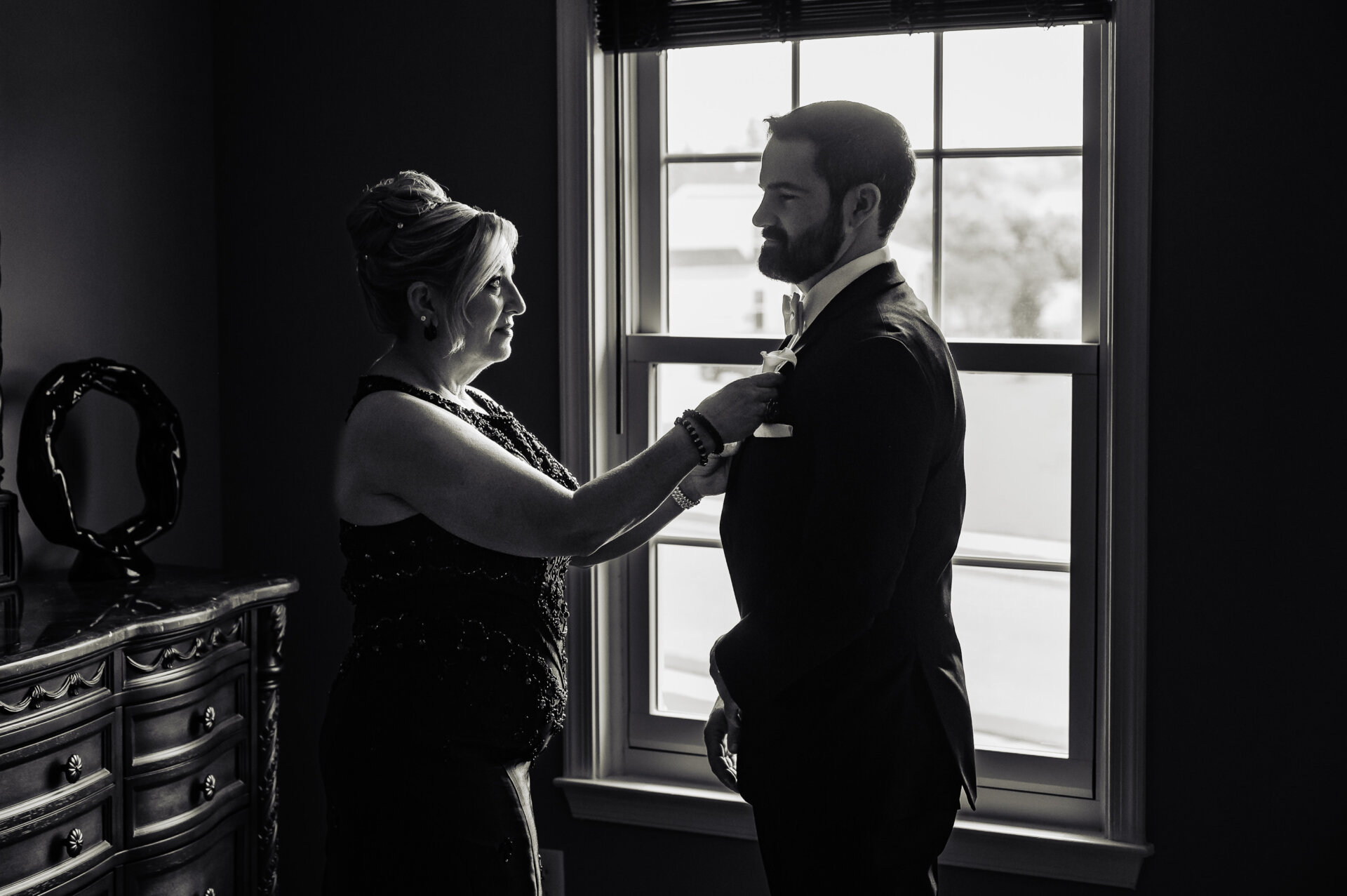 Mother placing a floral corsage on her son in suit jacket prior to ceremony