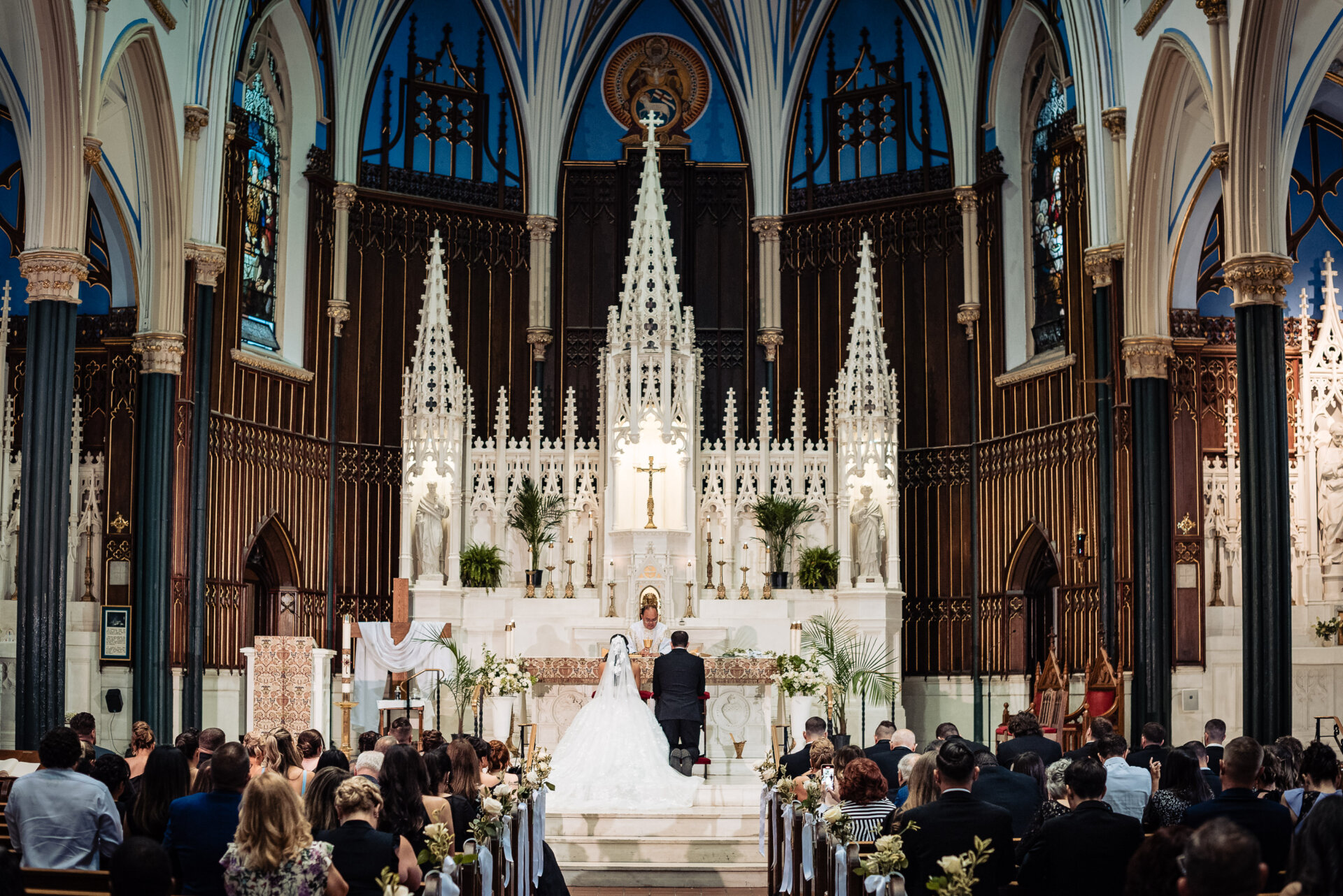 Wide view of the church interior with the couple kneeling at the altar during their wedding ceremony.