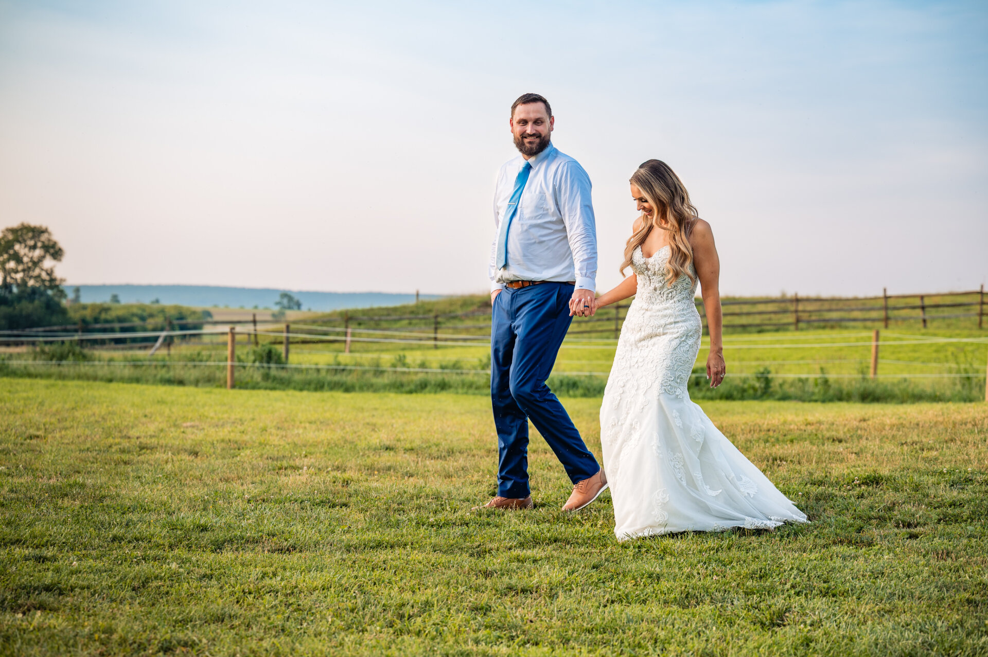 Bride and groom holding hands while walking across an open field during golden hour portraits.