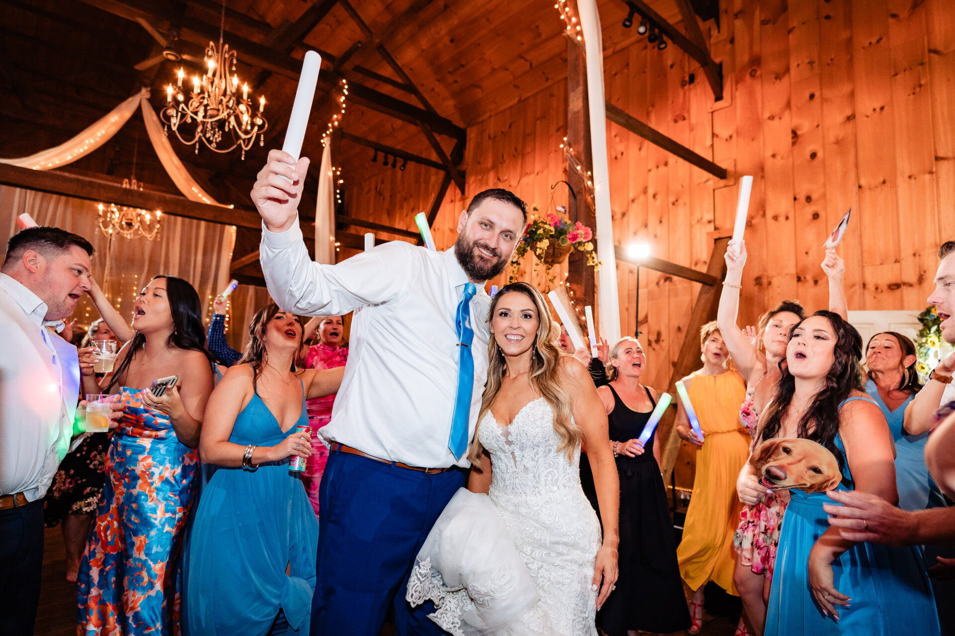 Bride and groom posing on the dance floor holding glow sticks as guests celebrate around them