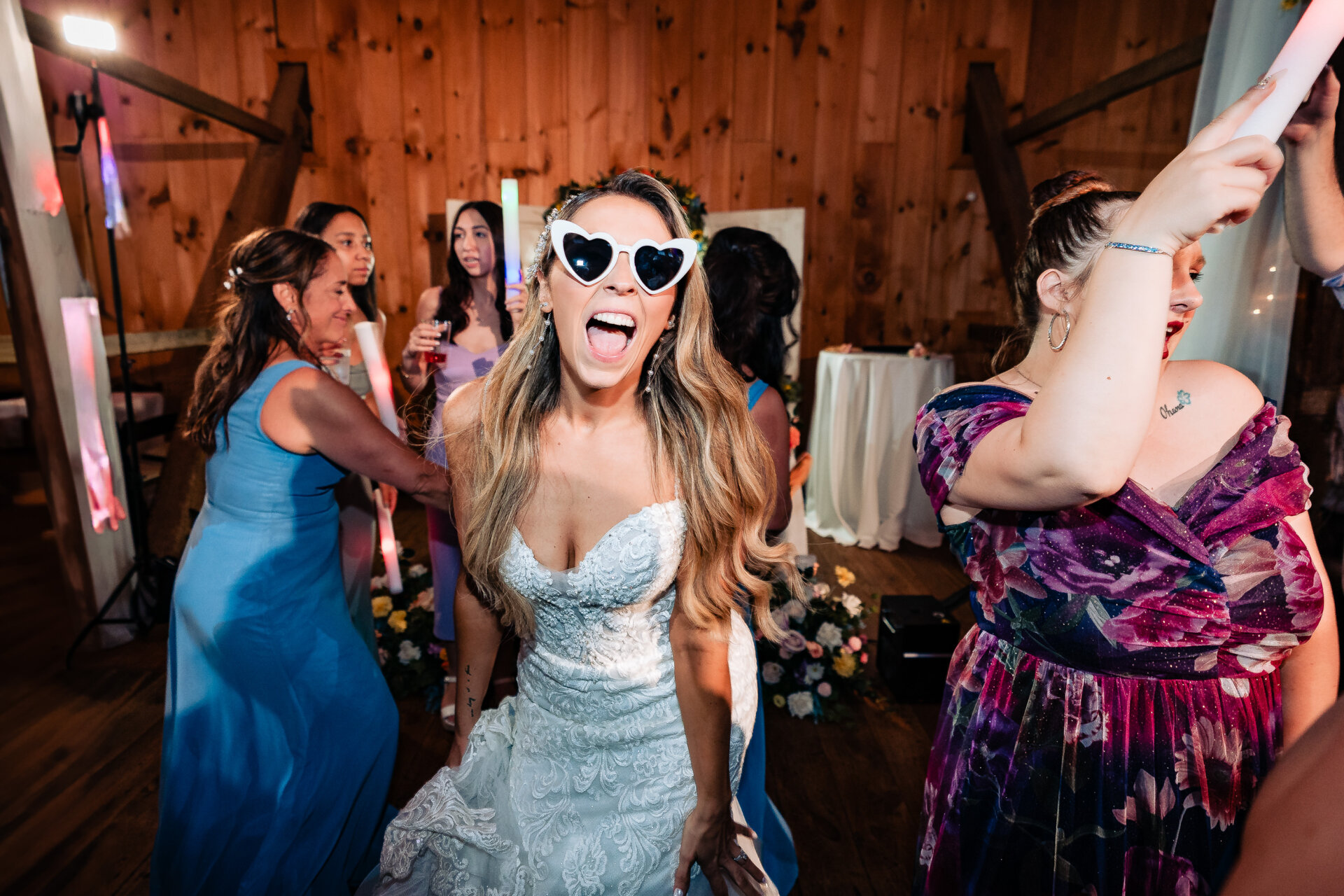 Bride dancing with friends on the dance floor wearing heart-shaped sunglasses during the wedding reception