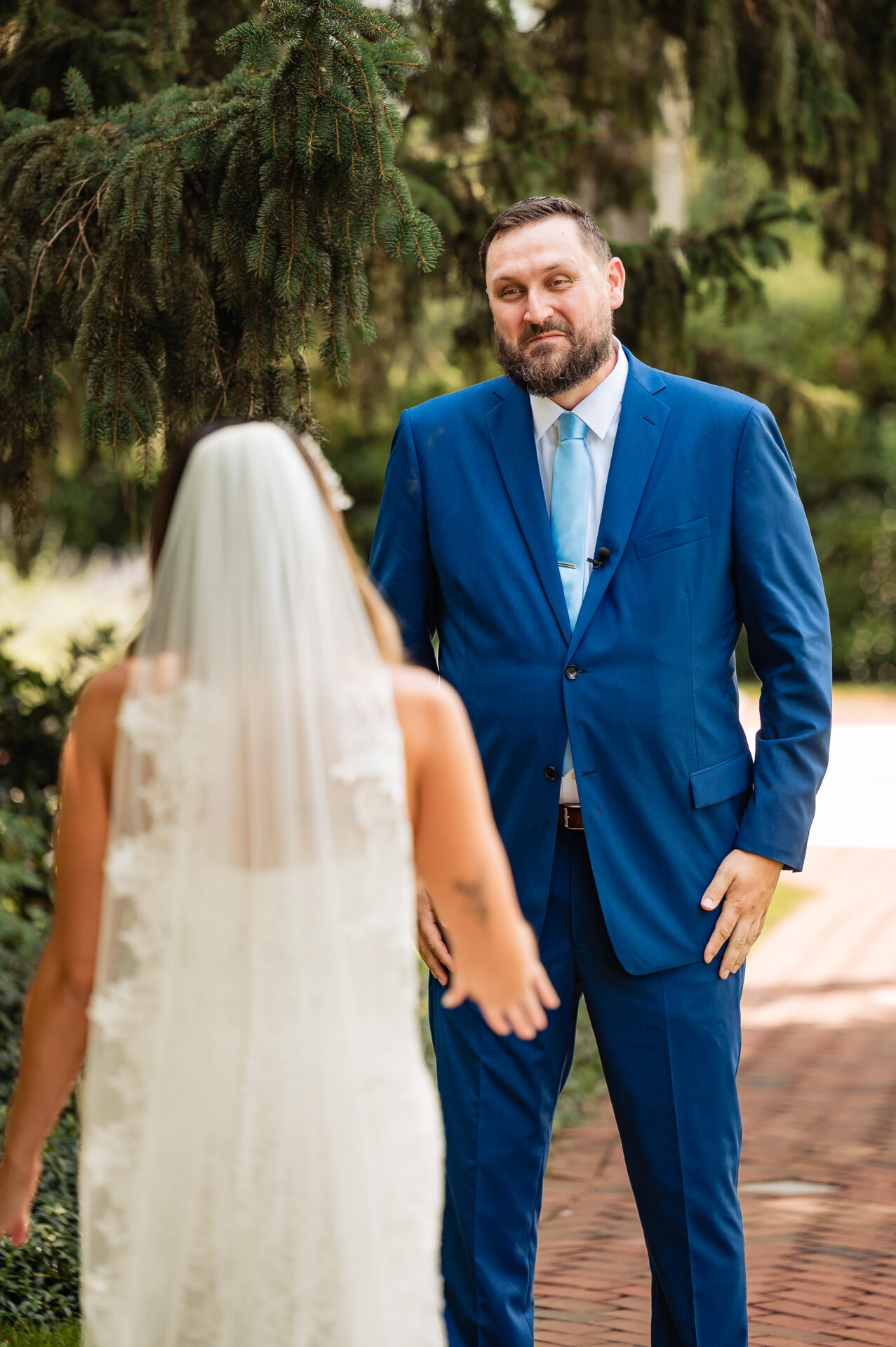 “Bride and groom share an emotional first look hug outdoors beneath evergreen trees on their wedding day.”