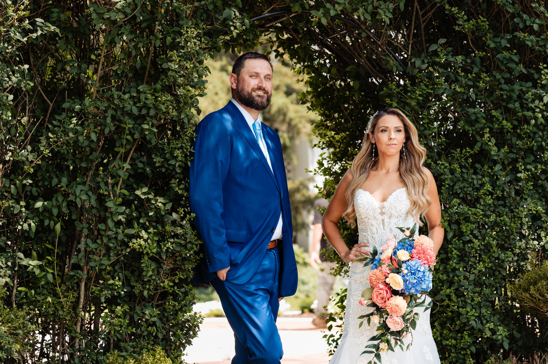 Bride and groom posing together in a garden with the bride holding a colorful floral bouquet.