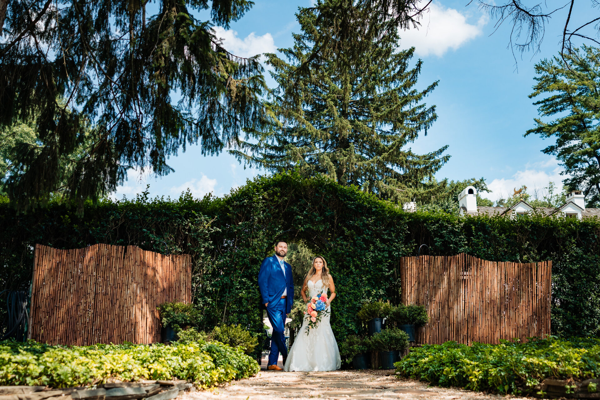Bride and groom standing together in a garden walkway, framed by greenery and trees at an outdoor wedding venue