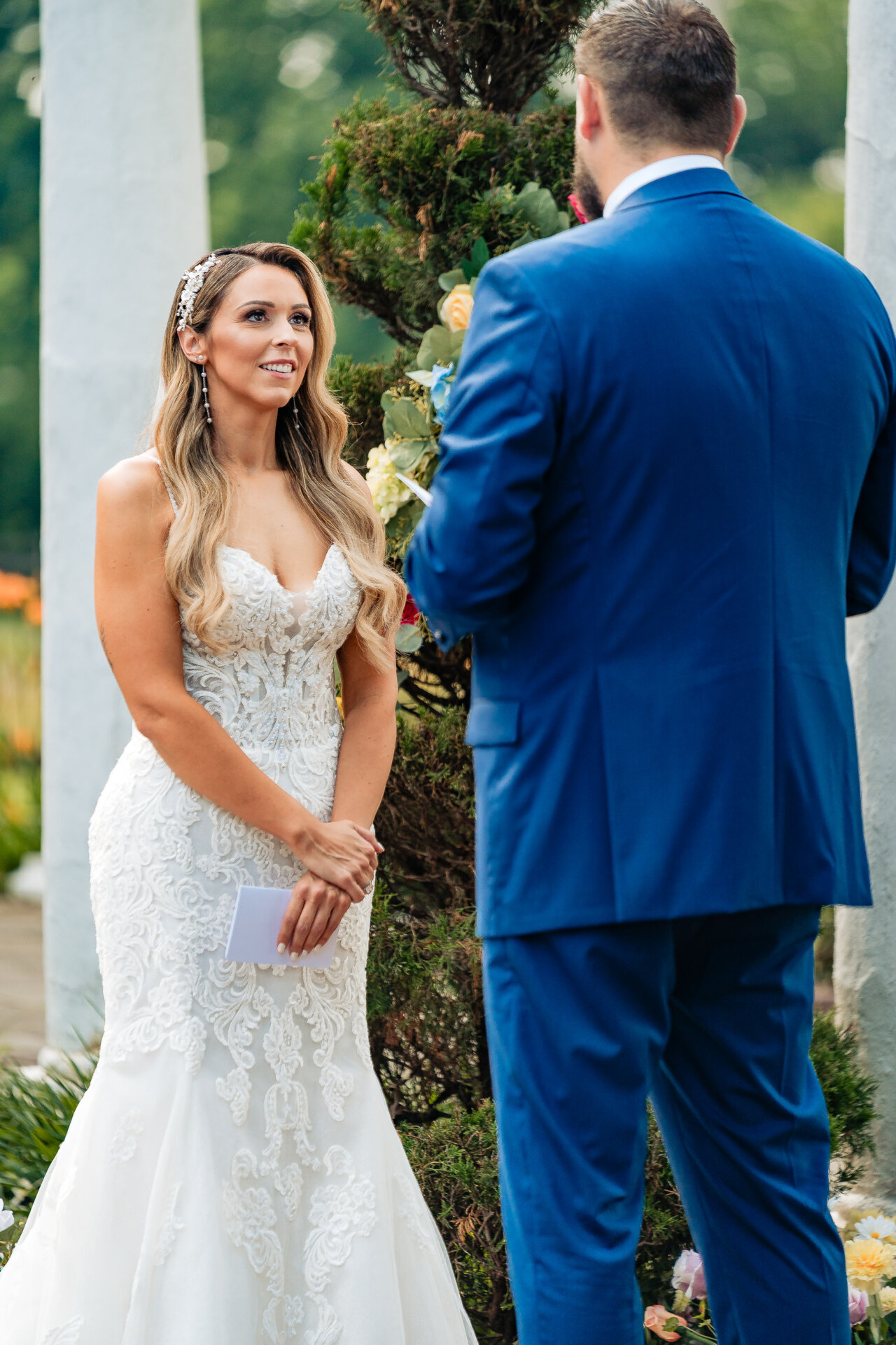 Bride and groom exchanging vows during an outdoor ceremony beneath greenery and floral decor