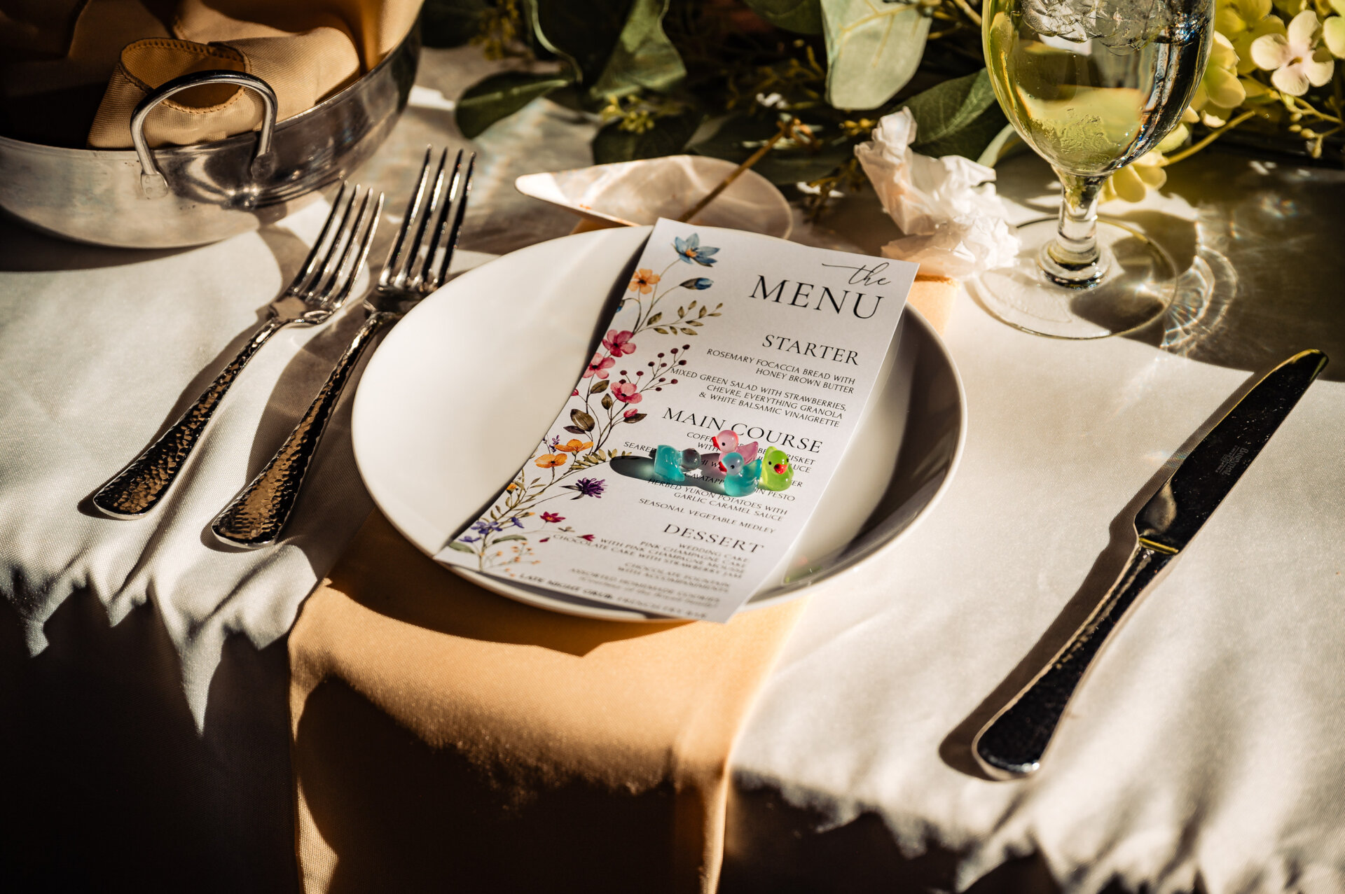 Close-up of a wedding place setting with a printed menu card, flatware, and glassware.