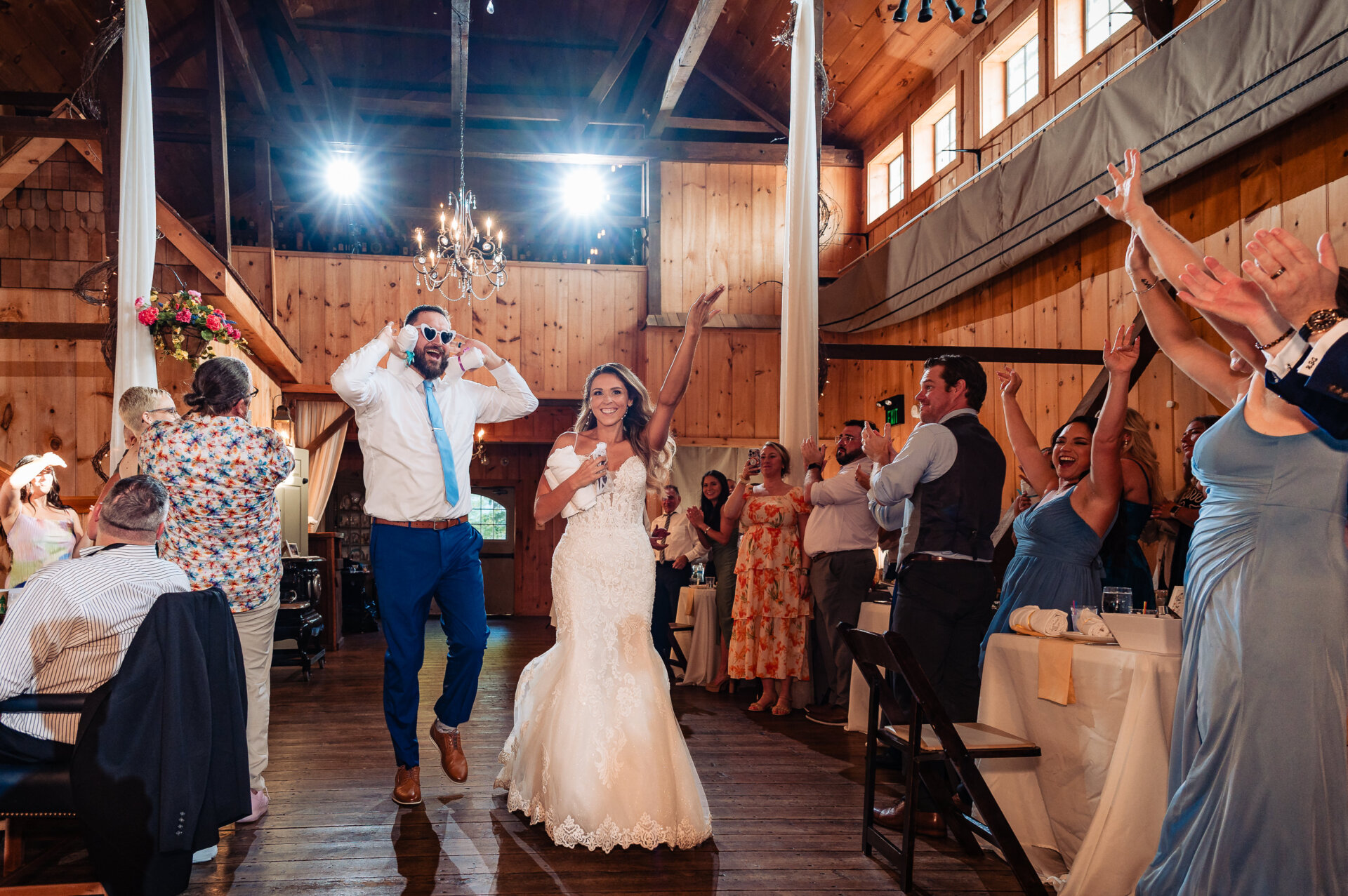 Bride and groom making a high-energy entrance into a rustic barn reception as guests cheer