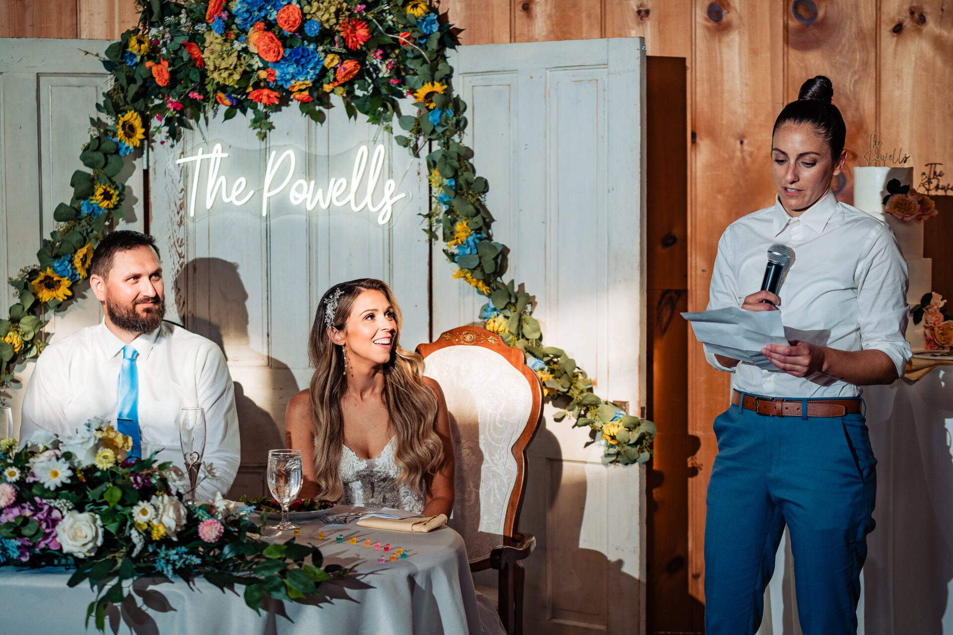Wedding toast being delivered as the bride and groom listen at their sweetheart table under floral decor