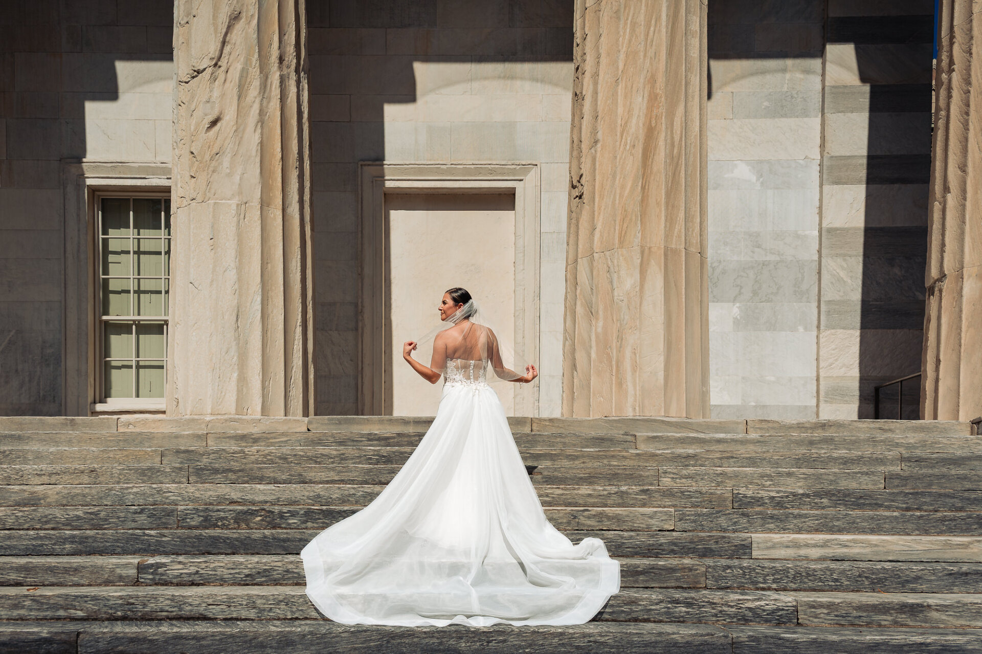 Bride with flowing train and veil standing on marble steps in front of neoclassical building with columns