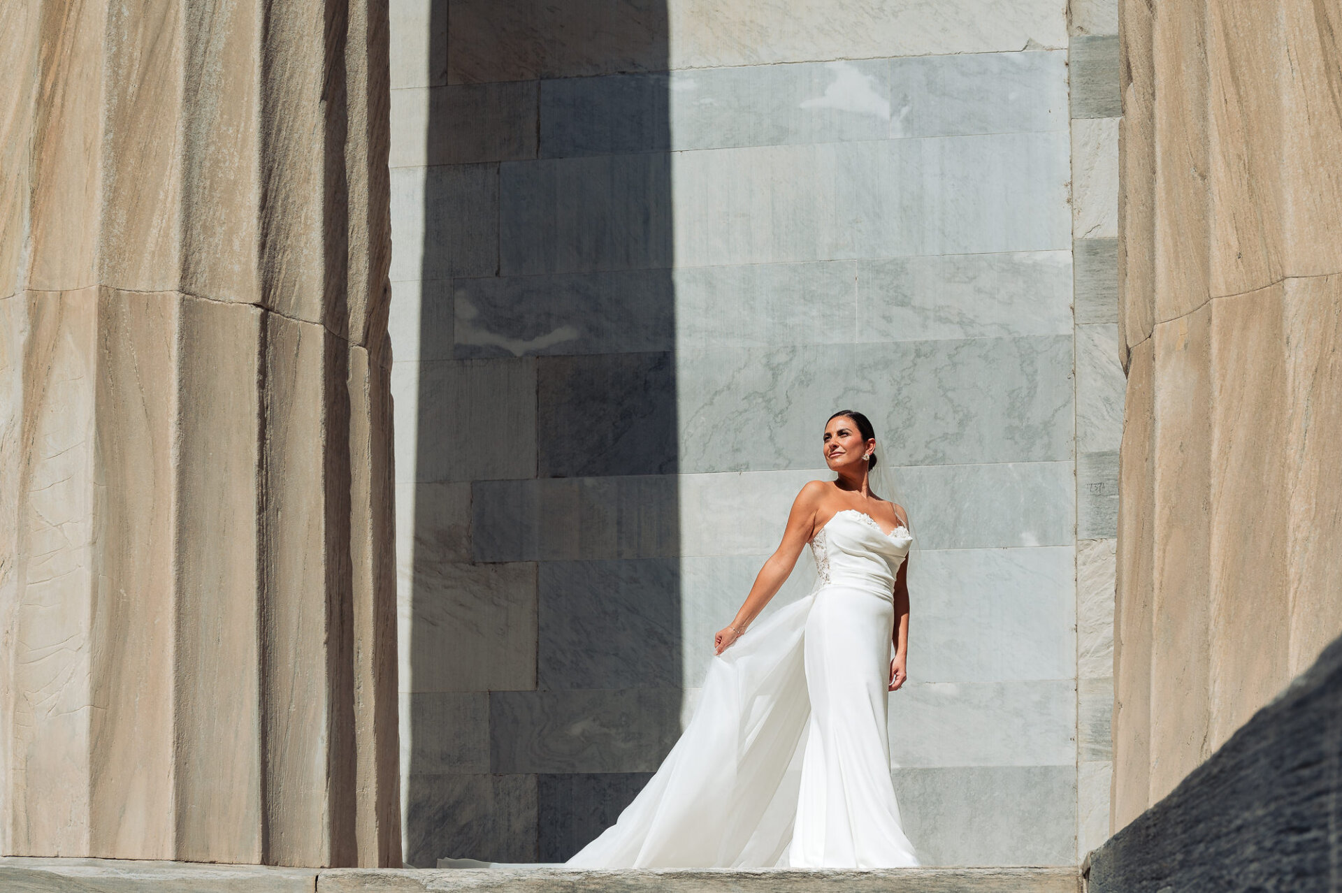 Bride in strapless white wedding gown twirling on marble steps in front of neoclassical building with tall columns