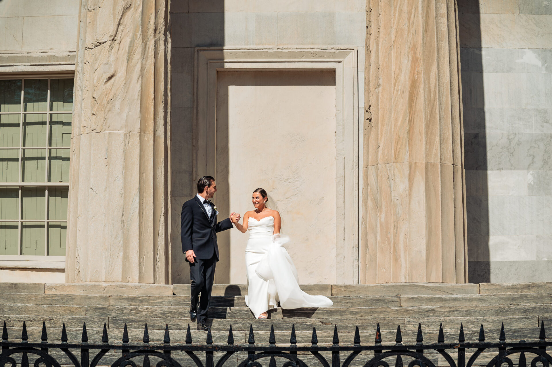 Bride and groom walking hand in hand between stone columns