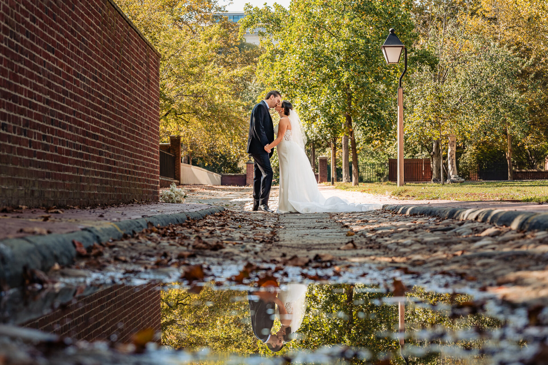 Bride and groom kissing on a cobblestone path with autumn trees at Union Trust