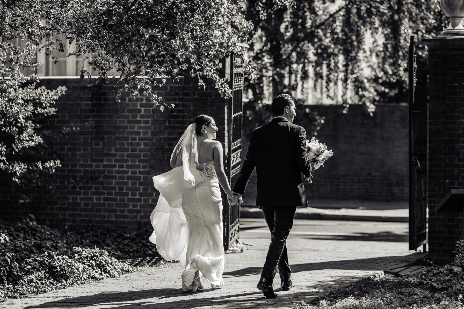 Black and white photo of bride and groom walking hand in hand through gates
