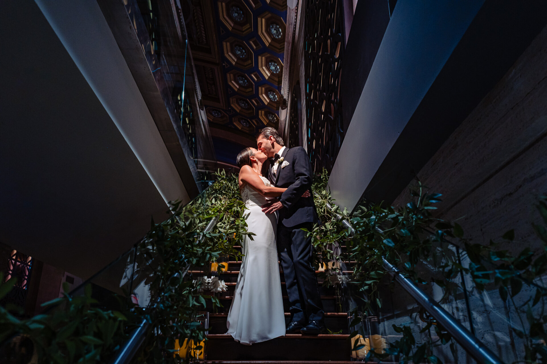 Bride and groom kissing on staircase with greenery at the Union Trust