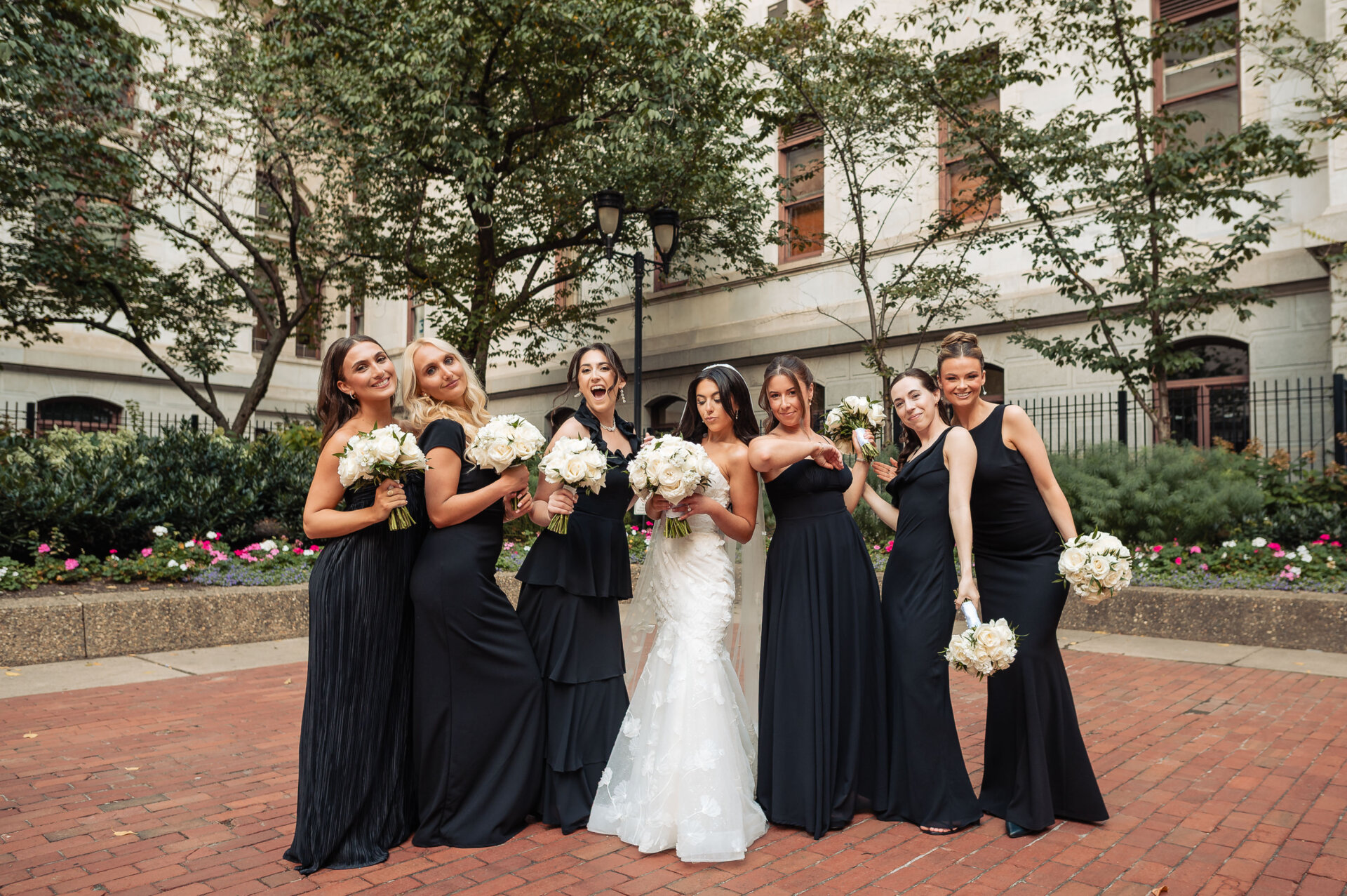 The bride posing with her bridesmaids, who are all wearing elegant black floor-length dresses and holding white bouquets.
