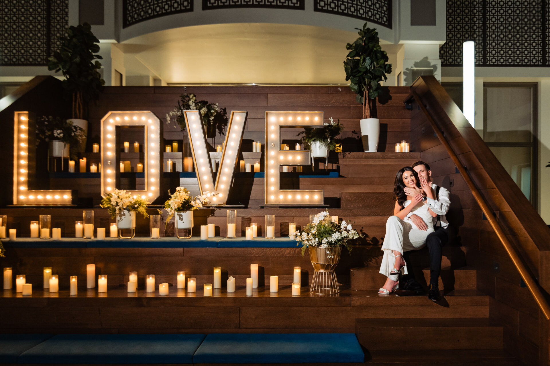 Bride and groom seated together beside illuminated LOVE marquee letters with candles and florals
