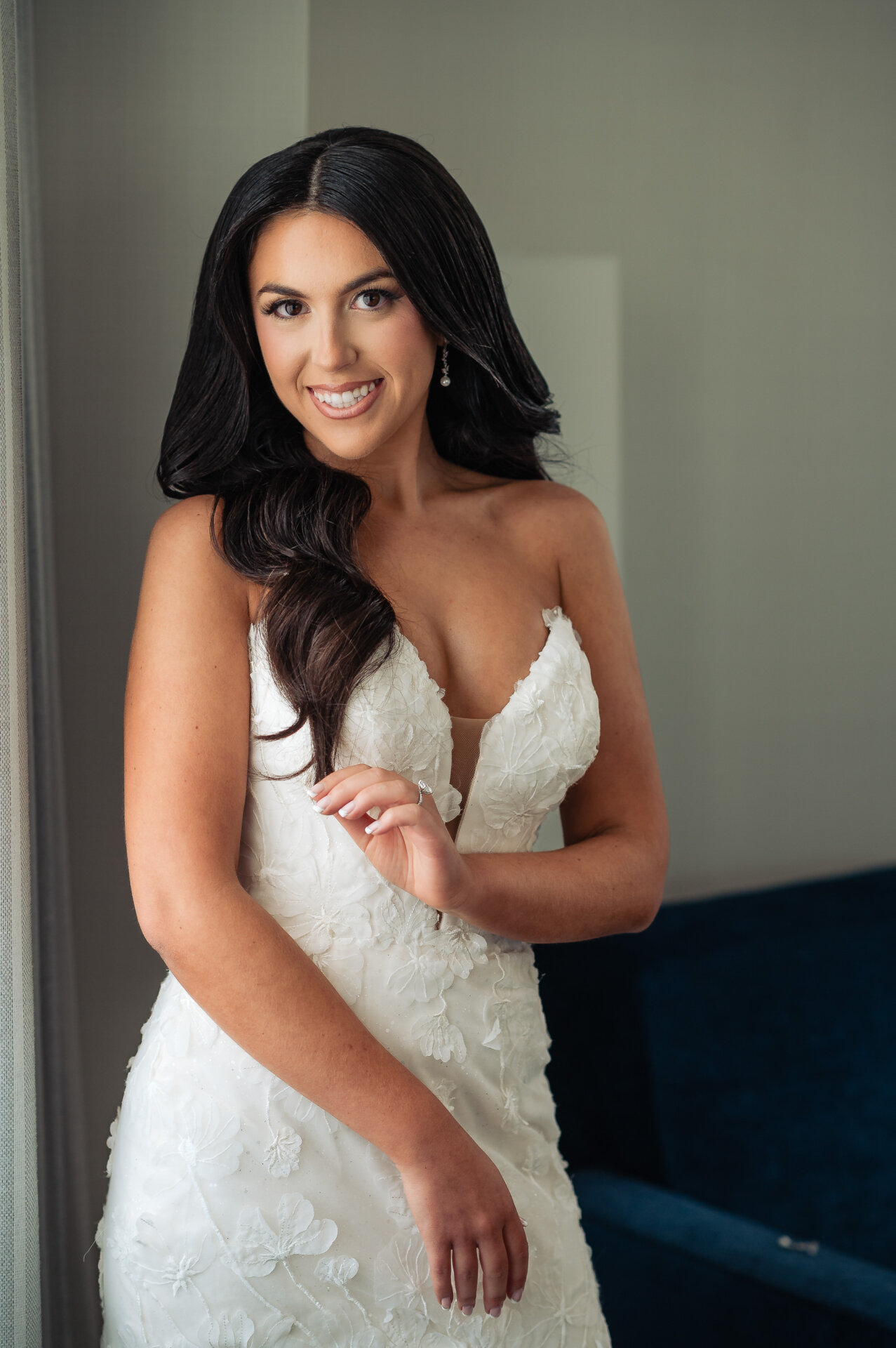 Bride smiling at camera in strapless white wedding gown with three-dimensional floral applique and long dark wavy hair