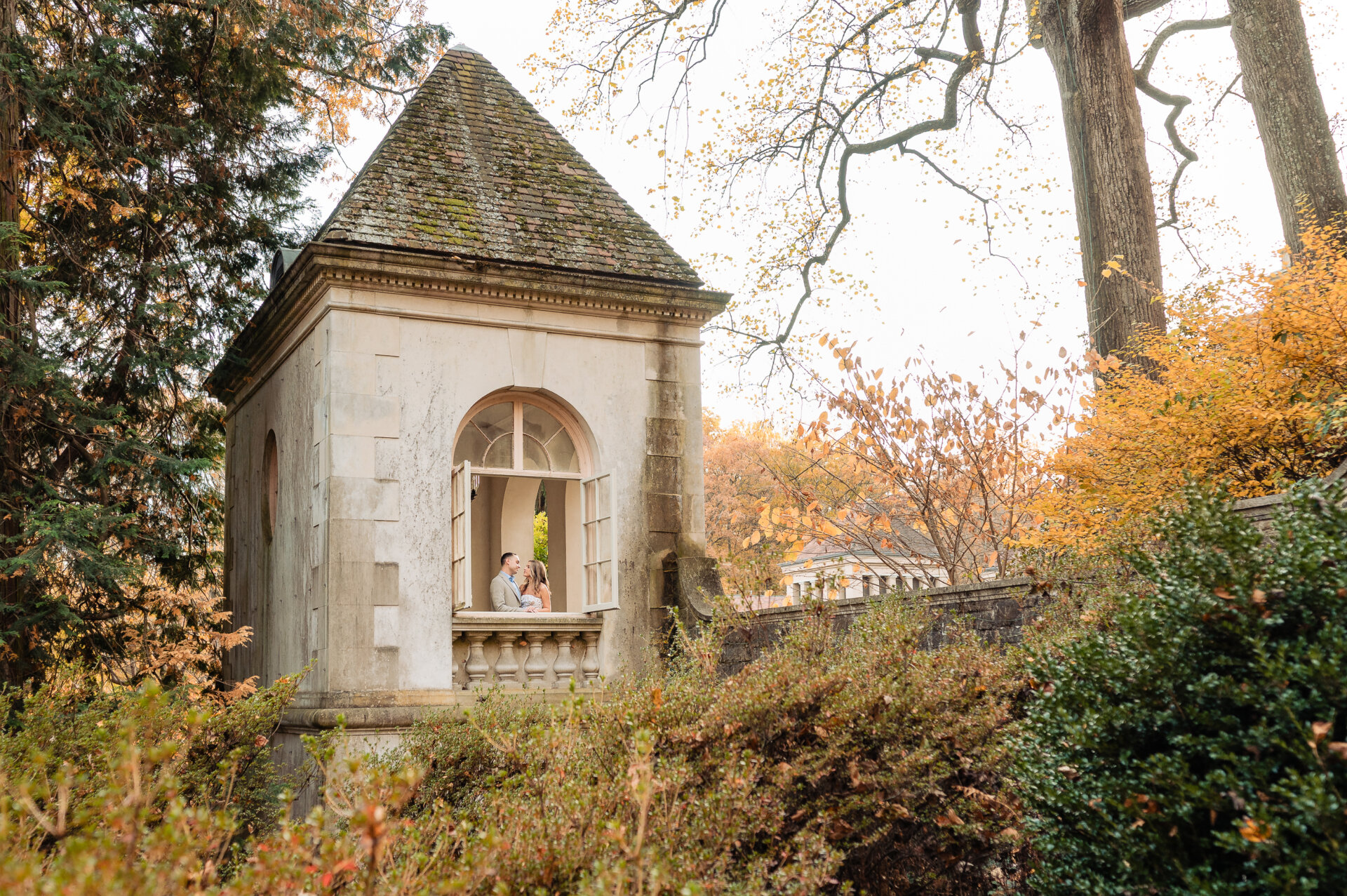 Couple standing by a stone pavilion surrounded by autumn foliage