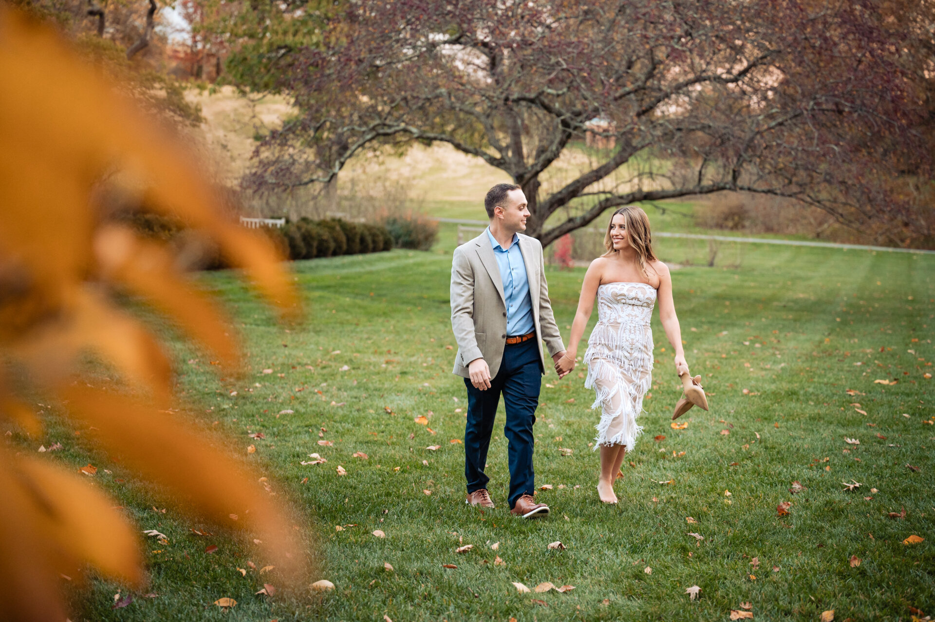 Engaged couple walking hand in hand across a grassy garden