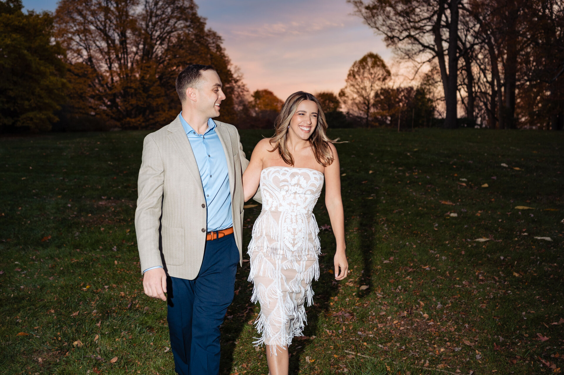 Couple strolling across a lawn at sunset during an engagement shoot
