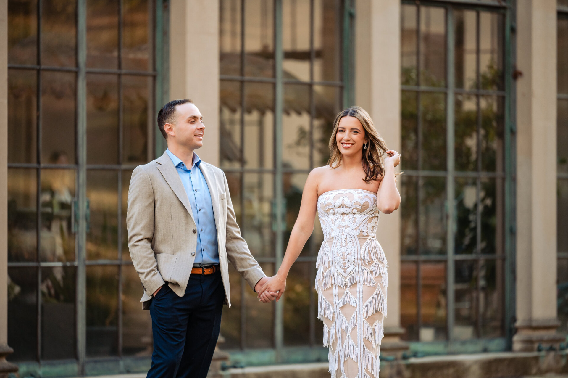 Engaged couple walking hand in hand past a conservatory building