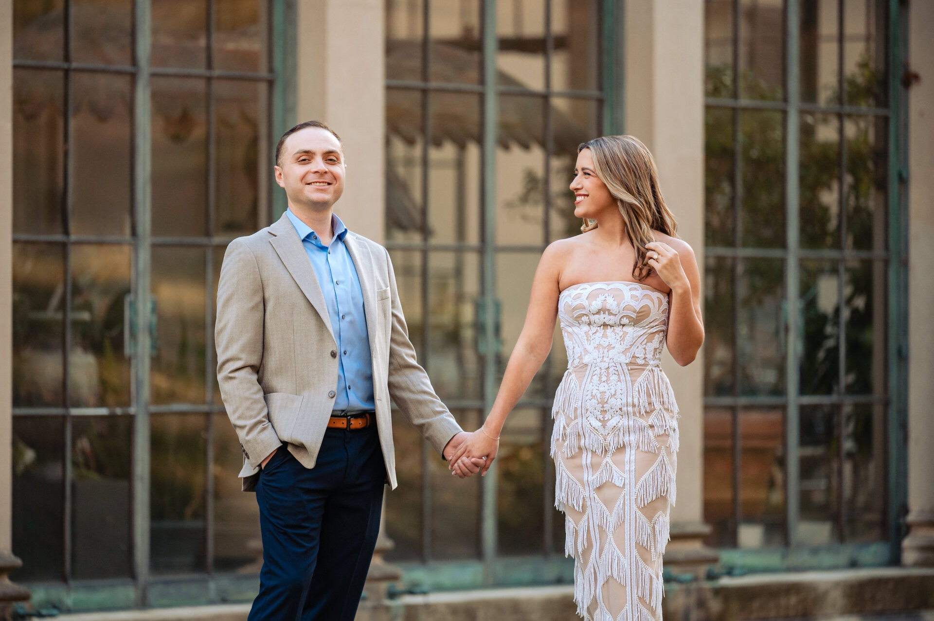 Engaged couple holding hands in front of a glass conservatory