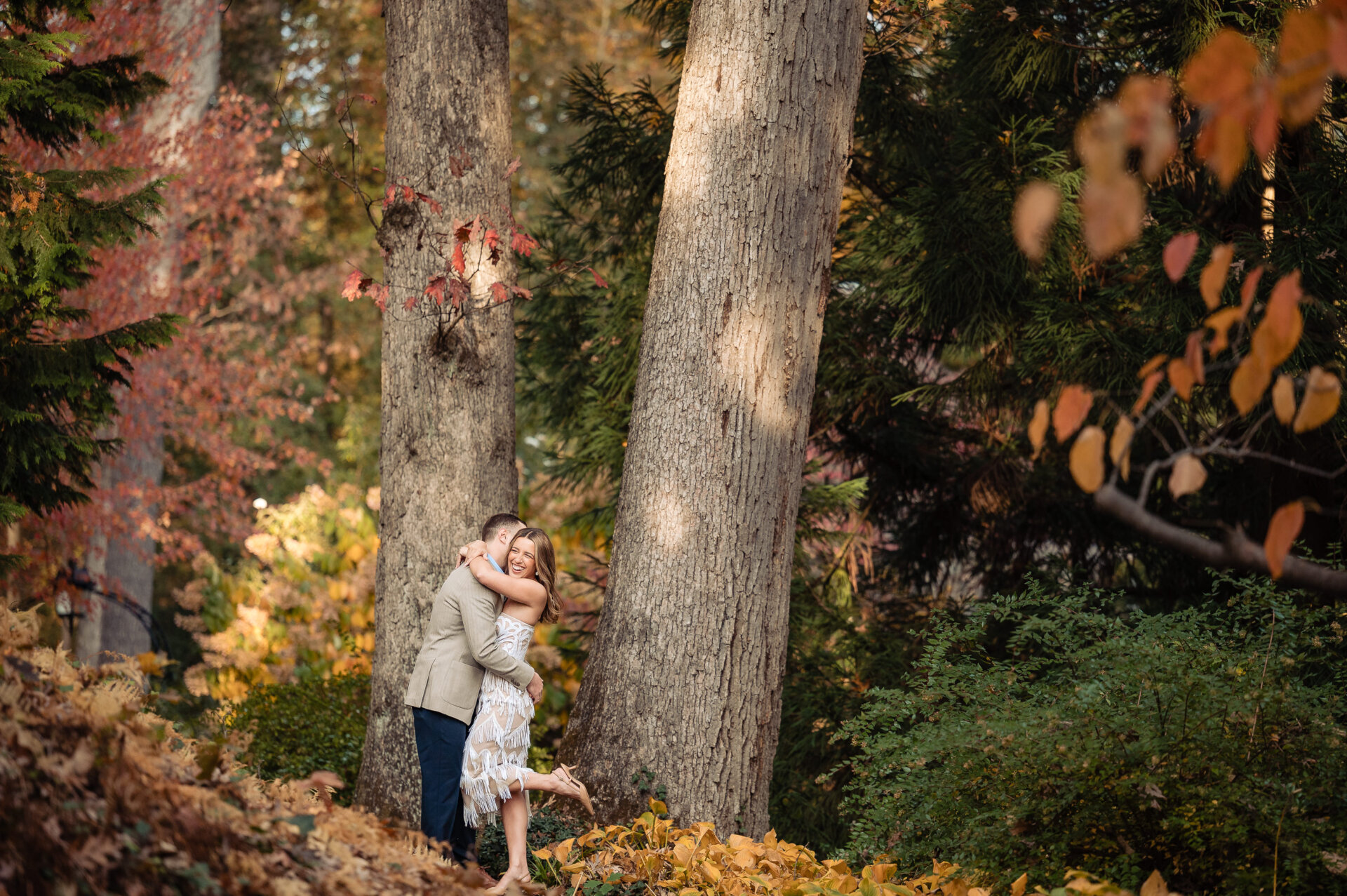 Couple embracing beneath tall trees during an autumn engagement session