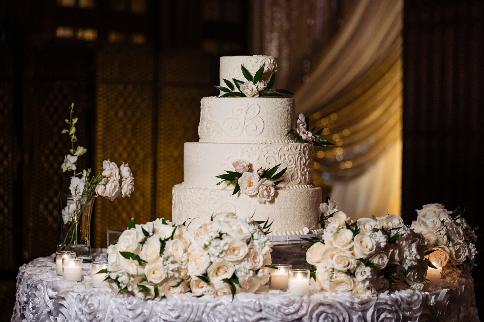 Four-tier white wedding cake with floral detailing displayed on a candlelit table inside the Crystal Tea Room