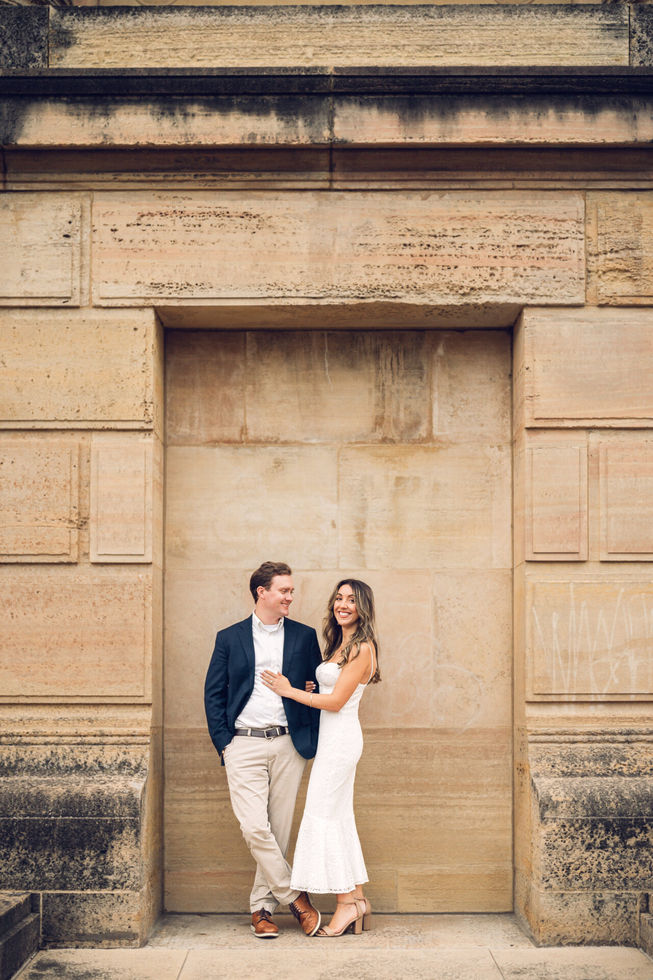 Engagement portrait of a couple leaning together against a historic stone wall.