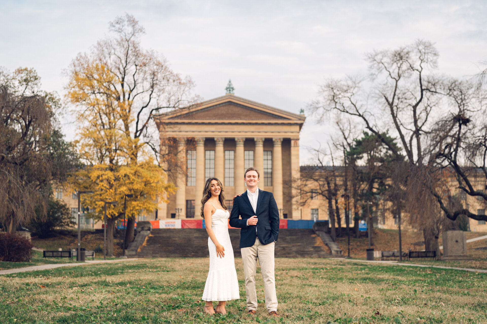 Engaged couple standing on the lawn in front of the Philadelphia Art Museum.