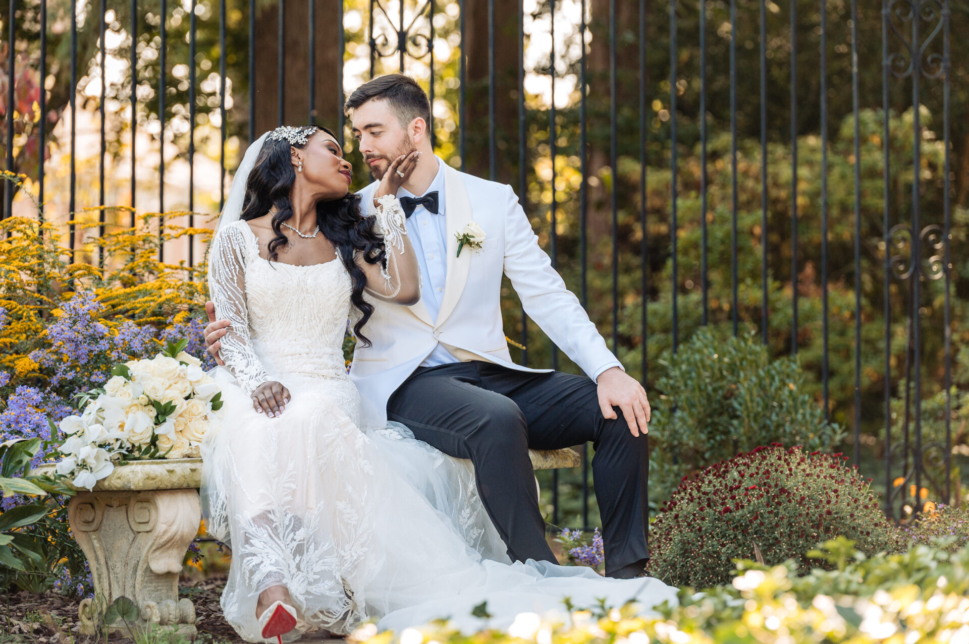 Bride and groom sitting together on rustic wooden bench in autumn forest with golden foliage and floral arrangements