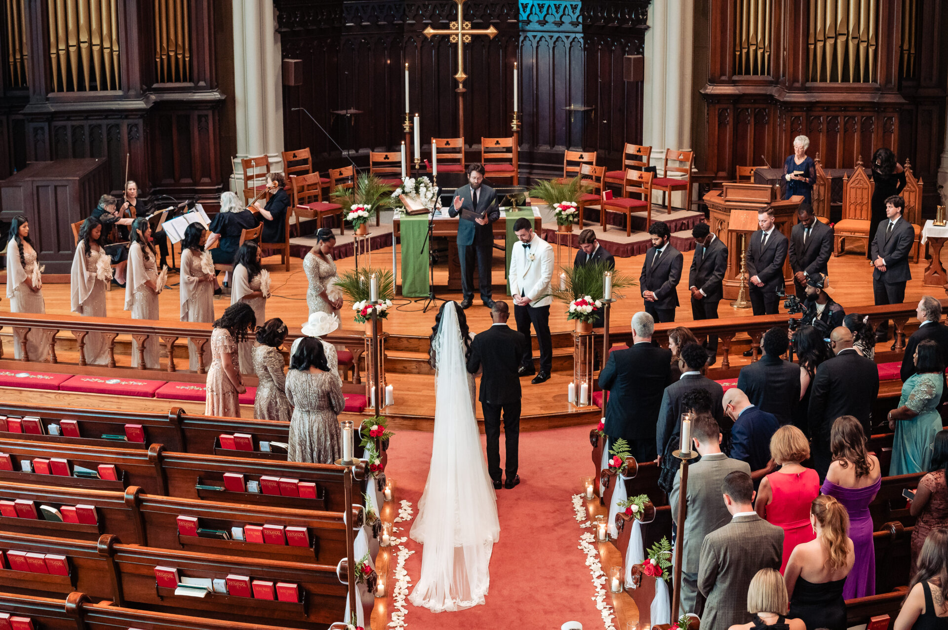 Wide view of a church wedding ceremony with the bride and groom facing the officiant as guests stand in the pews.