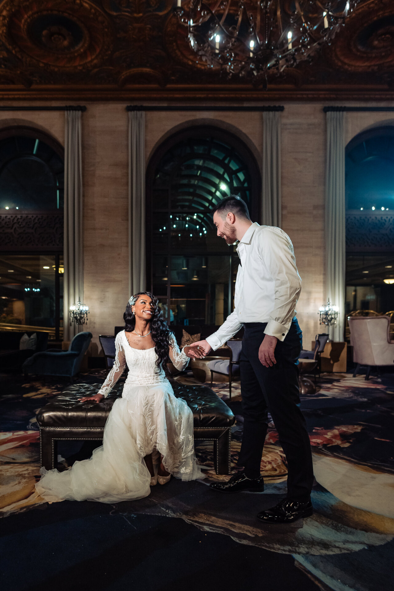 Groom holding the bride’s hand as she stands from a chair inside the Hotel DuPont lobby during evening portraits.