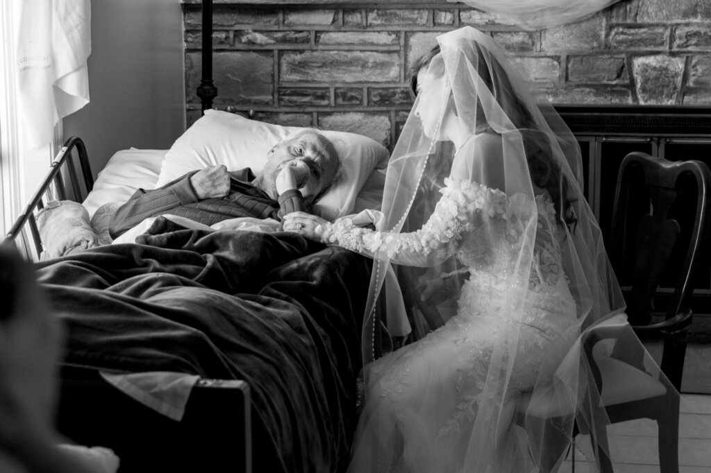 Black and white photo of the bride sitting beside her father on the bed with her veil draped over her before the ceremony.