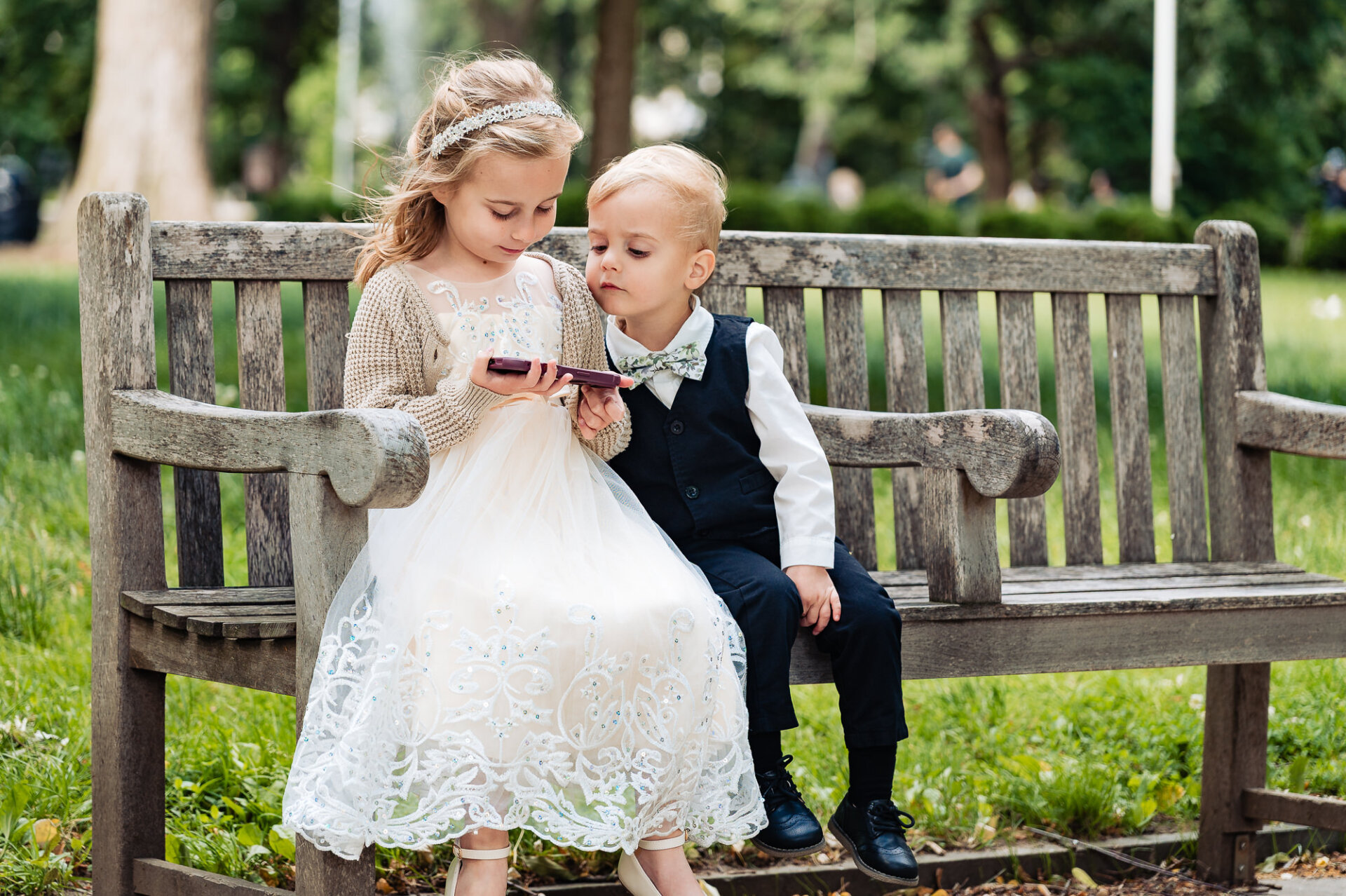 Flower girl and ring bearer sharing a quiet moment on a park bench before the ceremony