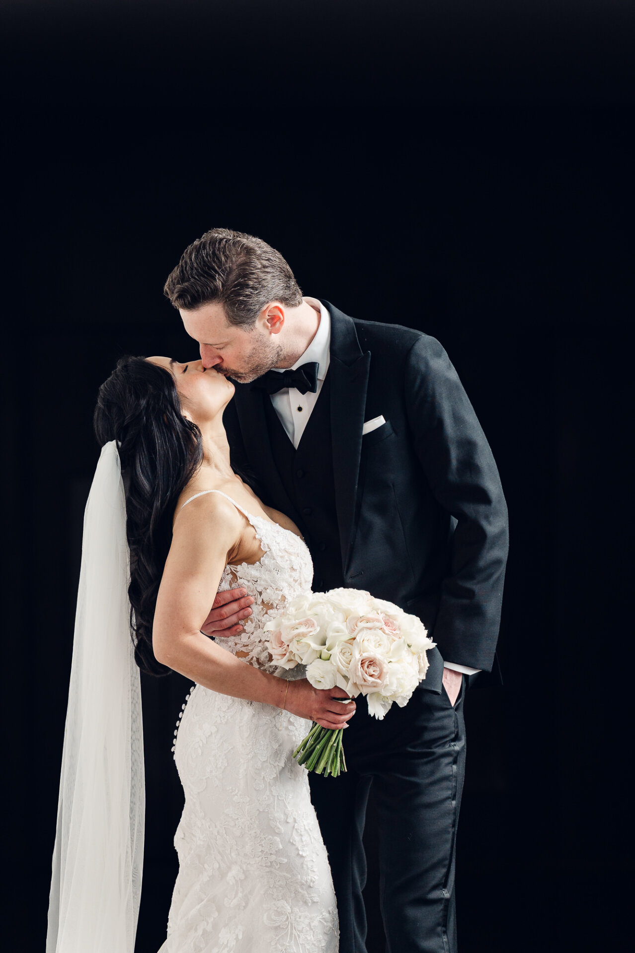 Classic wedding kiss portrait with a minimalist black backdrop and soft natural light