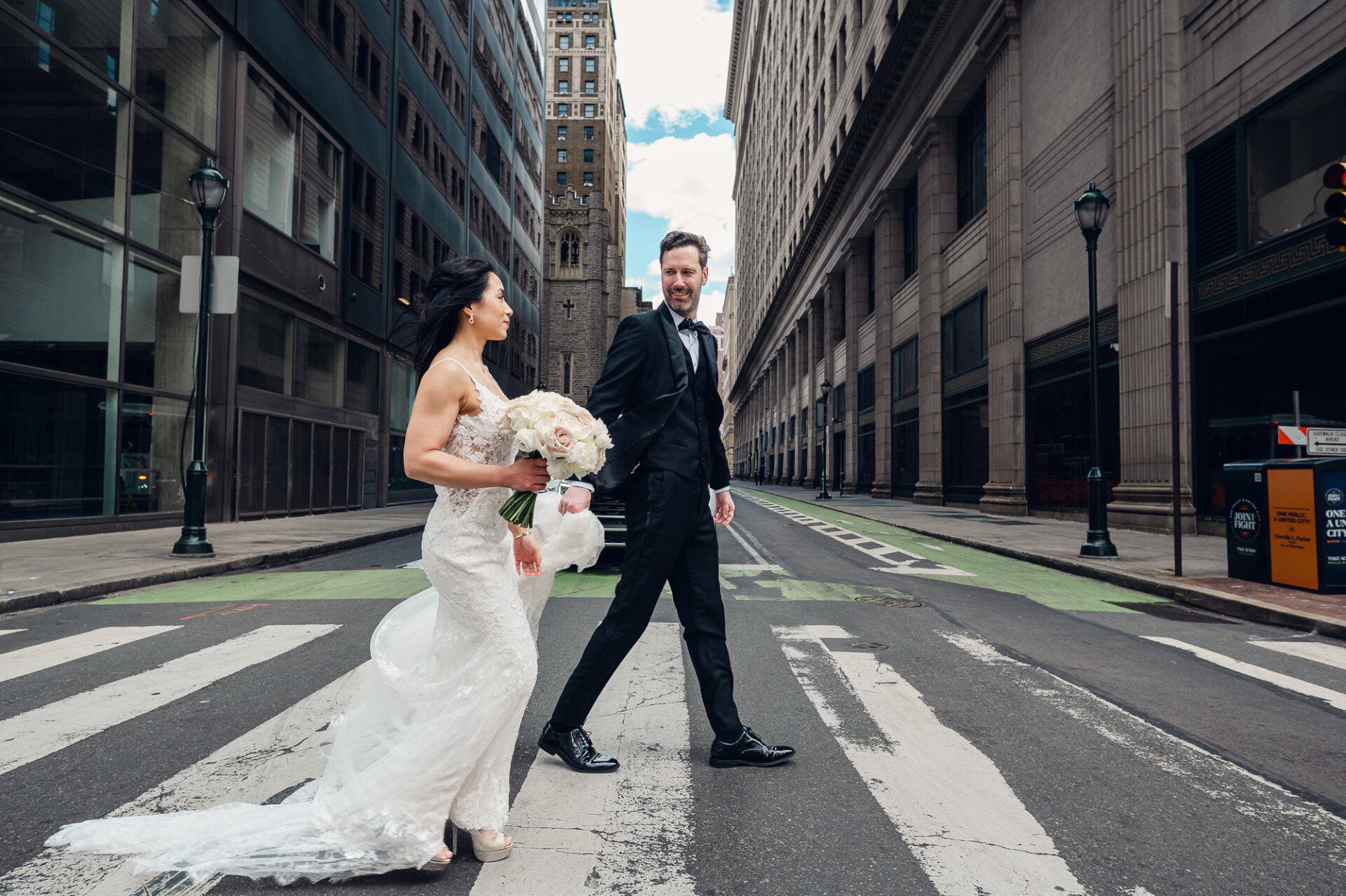 Newlyweds crossing a Philadelphia city street surrounded by historic architecture and urban views