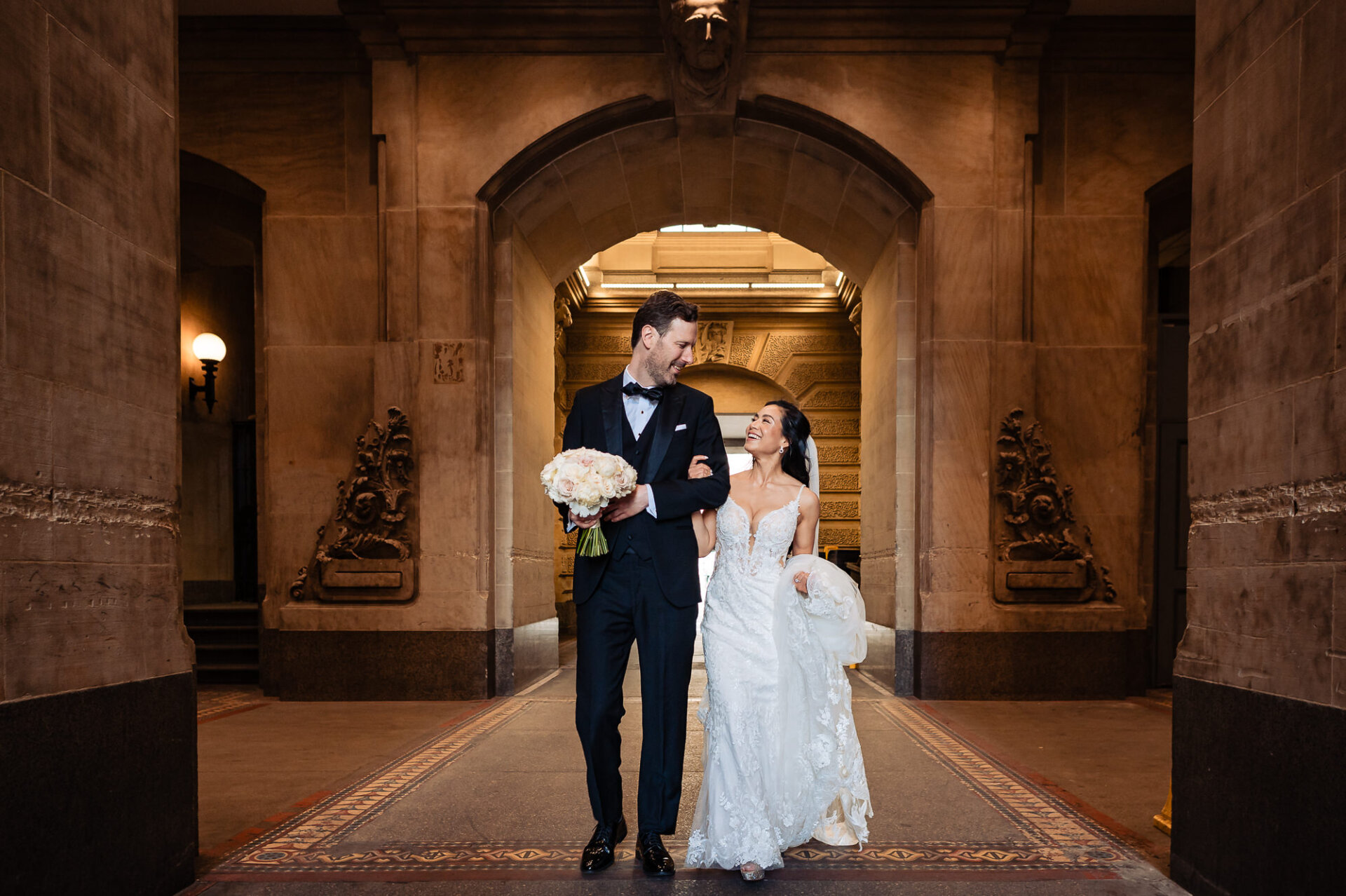 Bride and groom strolling arm in arm through Union Trust’s historic interior corridors