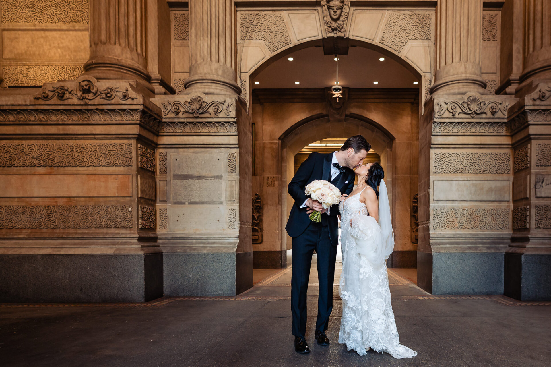 Romantic wedding kiss beneath ornate stone archways at Union Trust