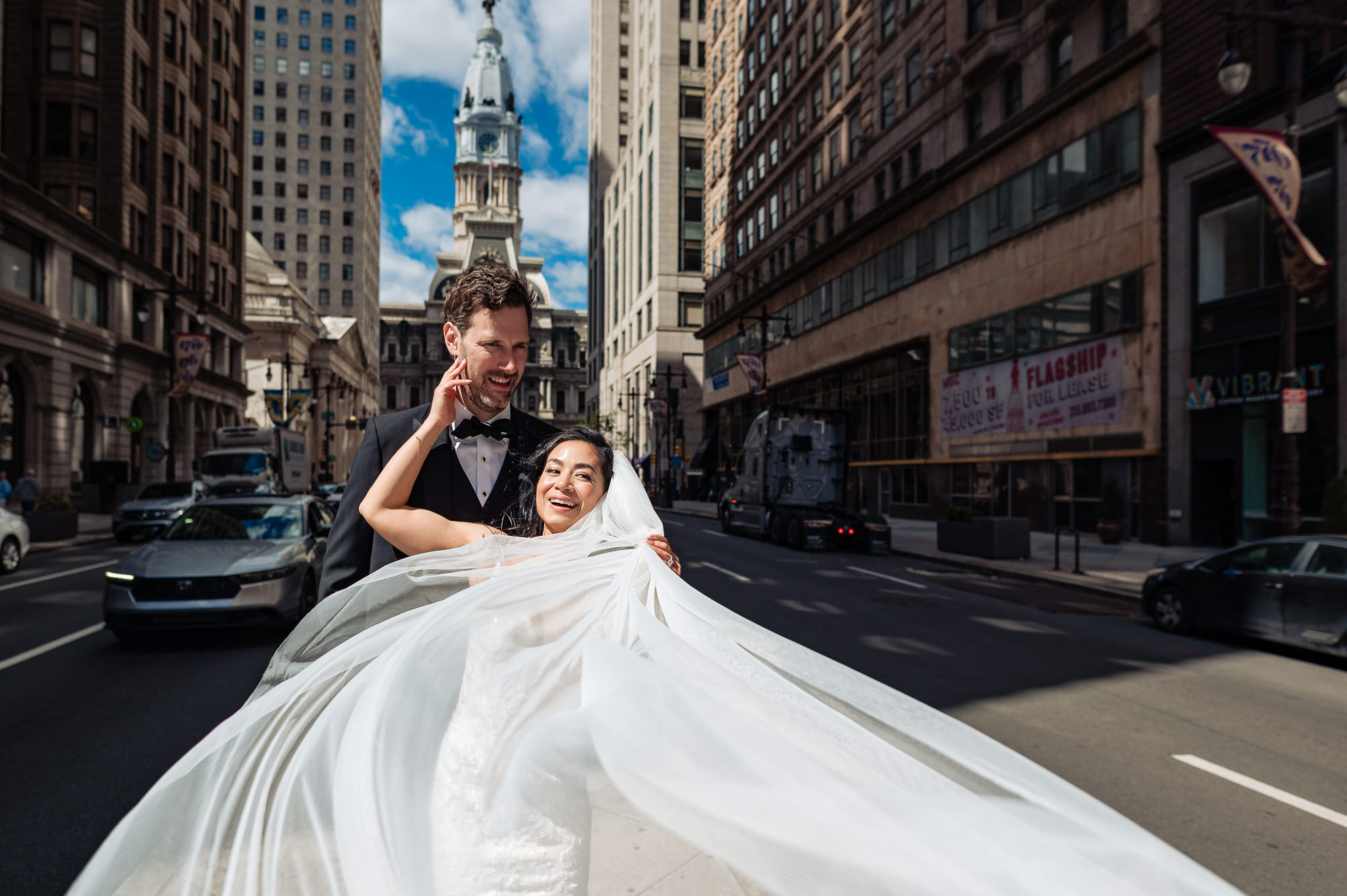 Playful downtown Philadelphia wedding portrait with a sweeping veil and city skyline views