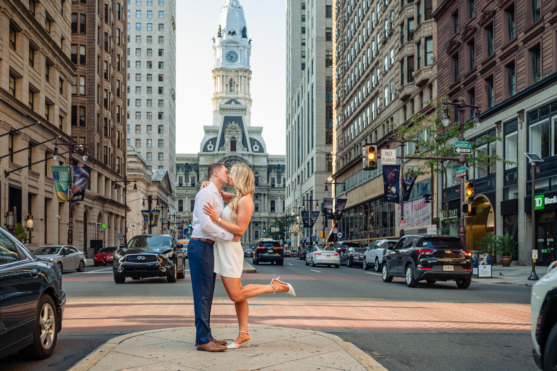 Bride popping leg while kissing groom in middle of Broad Street with Philadelphia City Hall tower centered in background