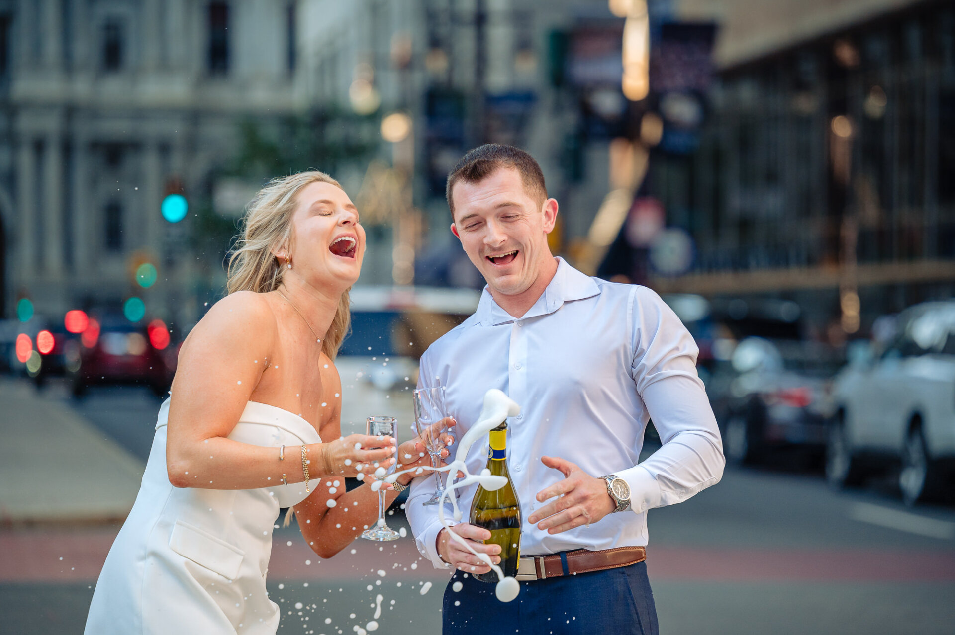 Bride reacting in surprise with open mouth as champagne fizzes over the bottle held by groom