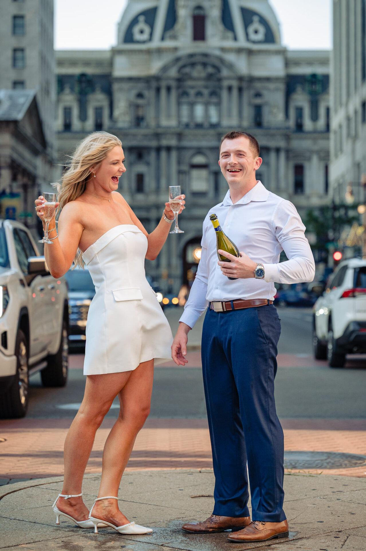Bride laughing with champagne glass raised while groom holds open bottle on Broad Street median