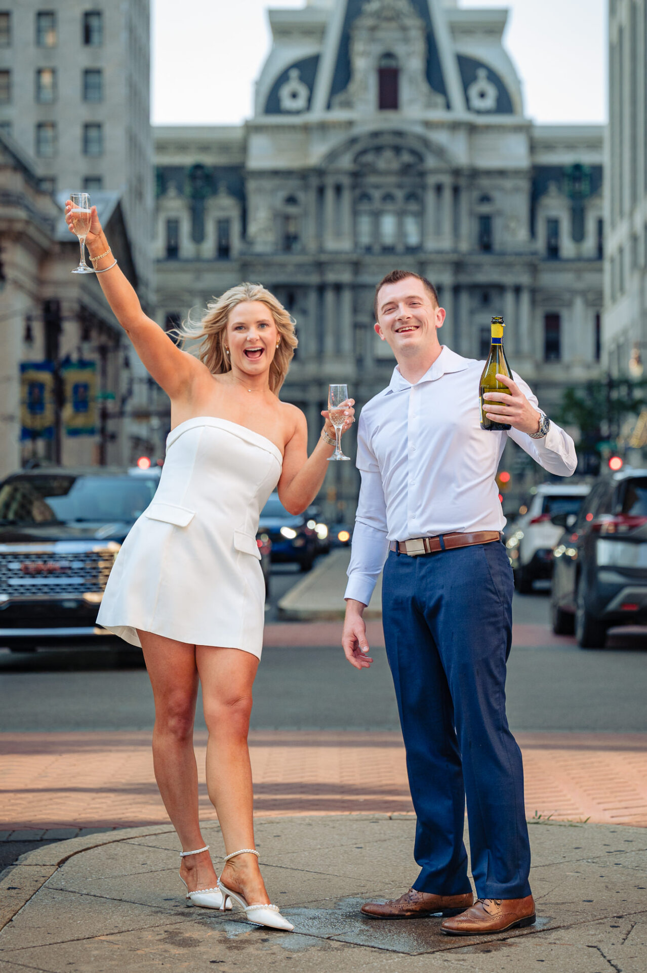 Groom popping champagne with a high foam spray as bride laughs during Center City Philadelphia engagement session