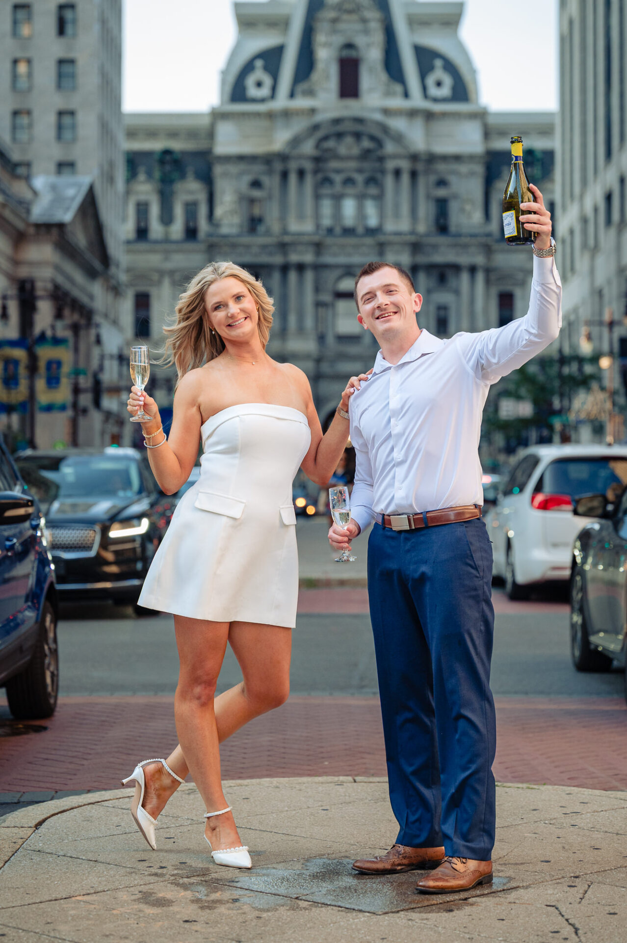 Groom popping champagne with a high foam spray as bride laughs during Center City Philadelphia engagement session