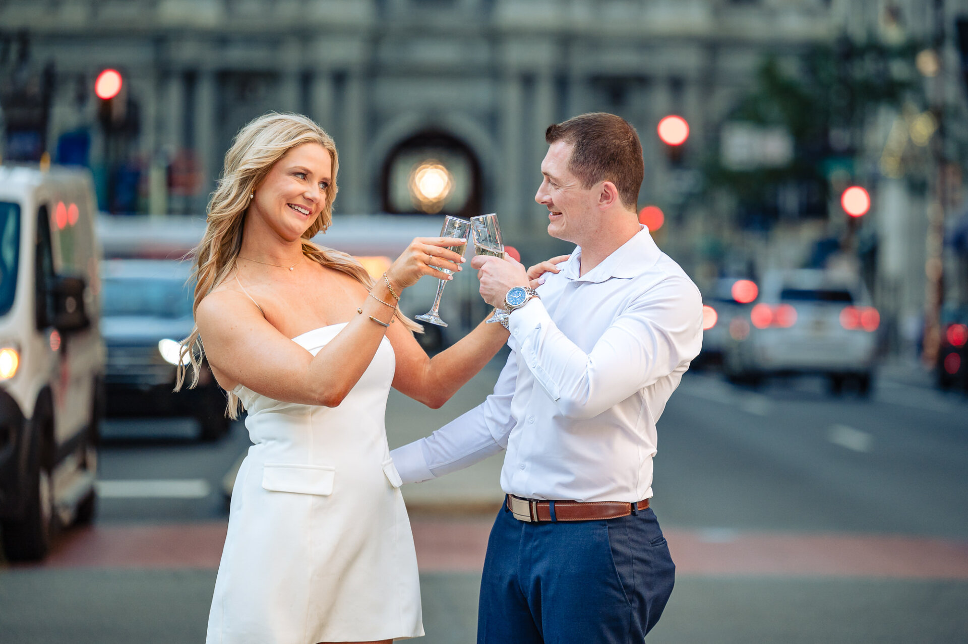 Engaged couple toasting champagne glasses on Broad Street in Center City Philadelphia at dusk